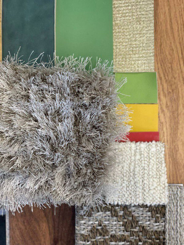 Подборка образцов материалов и текстур: ворсистый ковёр, образцы зелёных и горчичных тканей и природных фактур для оформления диванной и столовой зон проекта.