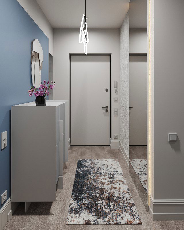 Продольный вид коридора: серая мебель у стены, ковер, входная дверь и отражение в зеркале, подчёркнутые мягким светом люстры.
