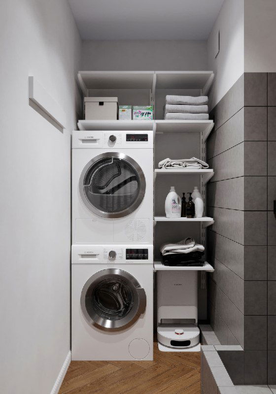 Прачечная зона с вертикально установленной стиральной и сушильной машинами, открытые полки с корзинами и роботом-пылесосом внизу.