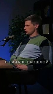 Гость подкаста в профиль: мужчина в свитере сидит у микрофона в студии; на кадре видна надпись «В НАЧАЛЕ ПРОШЛОЙ».