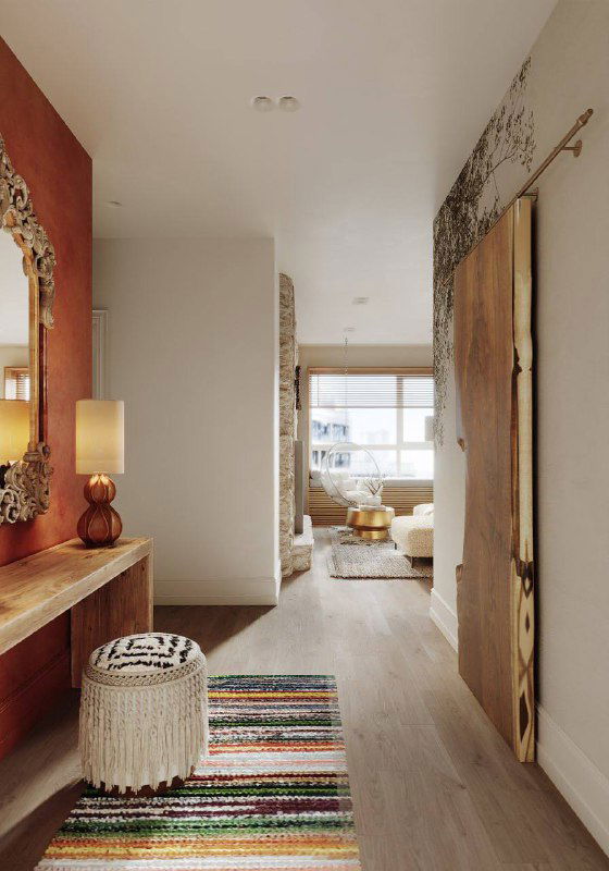 Вид узкой светлой прихожей: инженерная доска на полу, вязаный полосатый ковер у входа, пуф и открытая перспектива в жилую зону.
