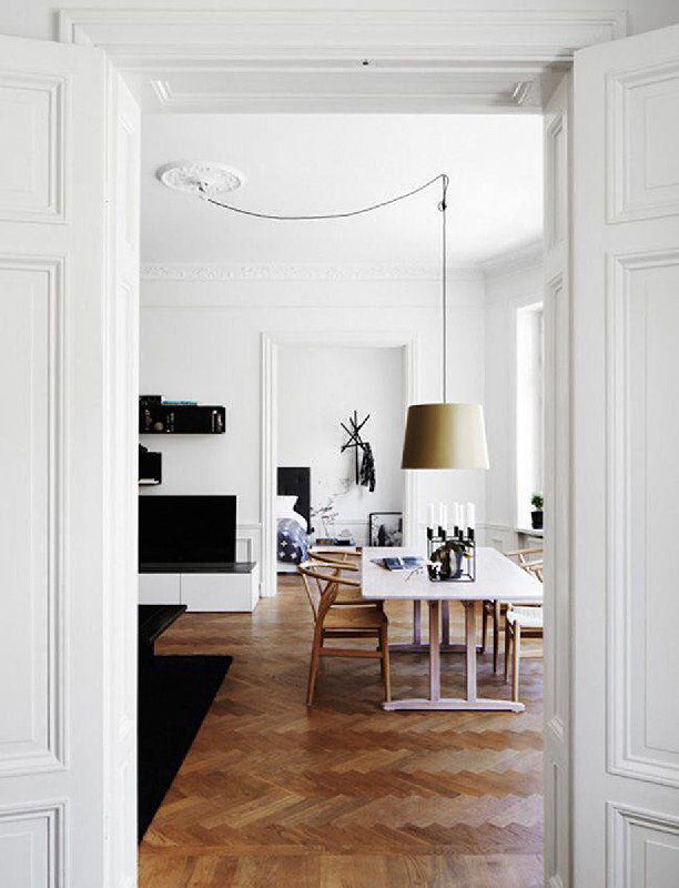 Светлая столовая с одиночной подвесной лампой и декоративной проводкой на потолке, белые двери и паркет создают спокойный скандинавский фон.