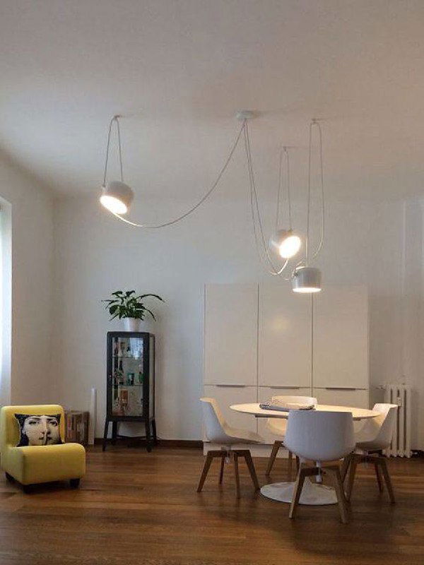 Белая гостиная с несколькими подвесными светильниками на длинных проводах; минималистичный интерьер и акцент на линии проводки.