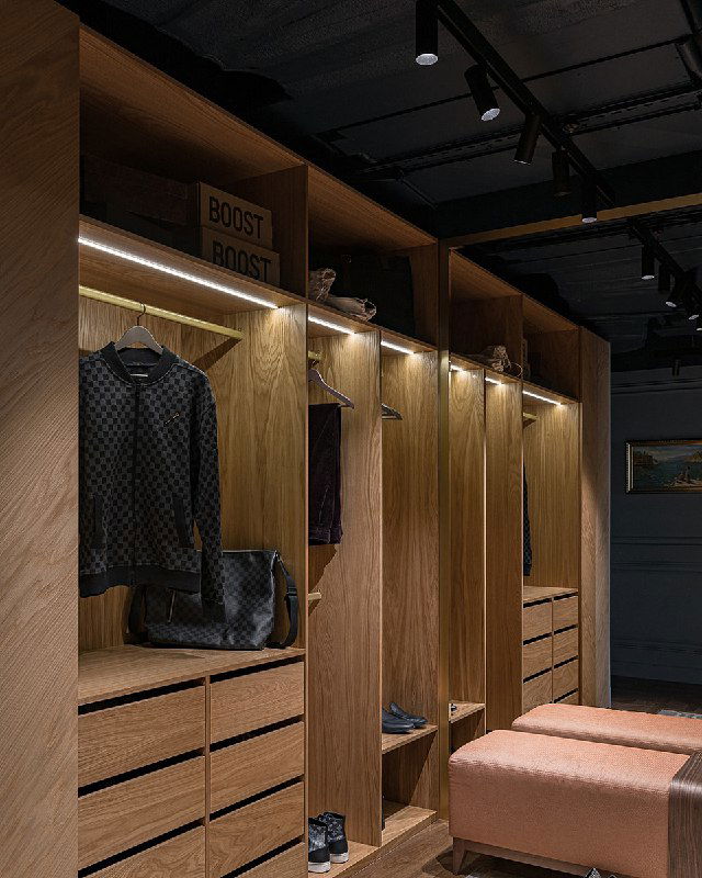 Детальный кадр системы хранения: полки и ящики из медового дерева, сумка на полке и направленные потолочные светильники на фоне чёрного потолка.