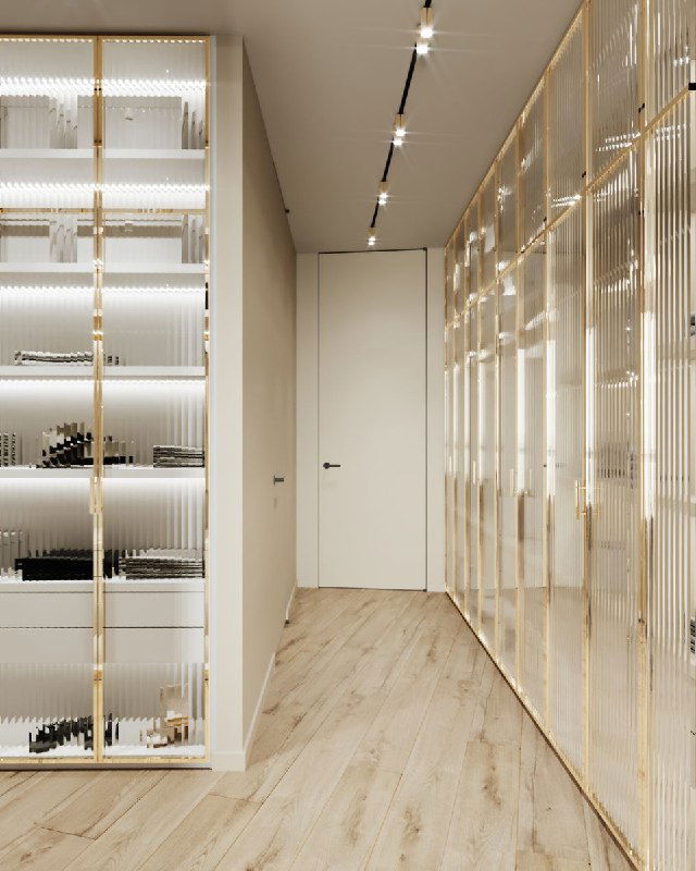 Узкий проход гардеробной с напольным покрытием светлого дерева и встроенными шкафами с глянцевыми фасадами и подсветкой для удобства хранения.