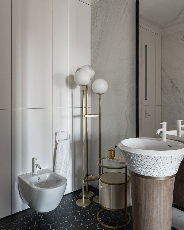 Угол ванной с биде, тонкая приставная тумба и золотой торшер Eichholtz на фоне панелей и мраморной отделки — акцент роскоши в интерьере.