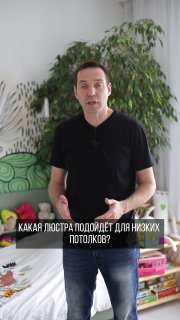 Дизайнер Иван Безруков в квартире на фоне полки с игрушками и большого зеленого растения — иллюстрация совета по люстре.