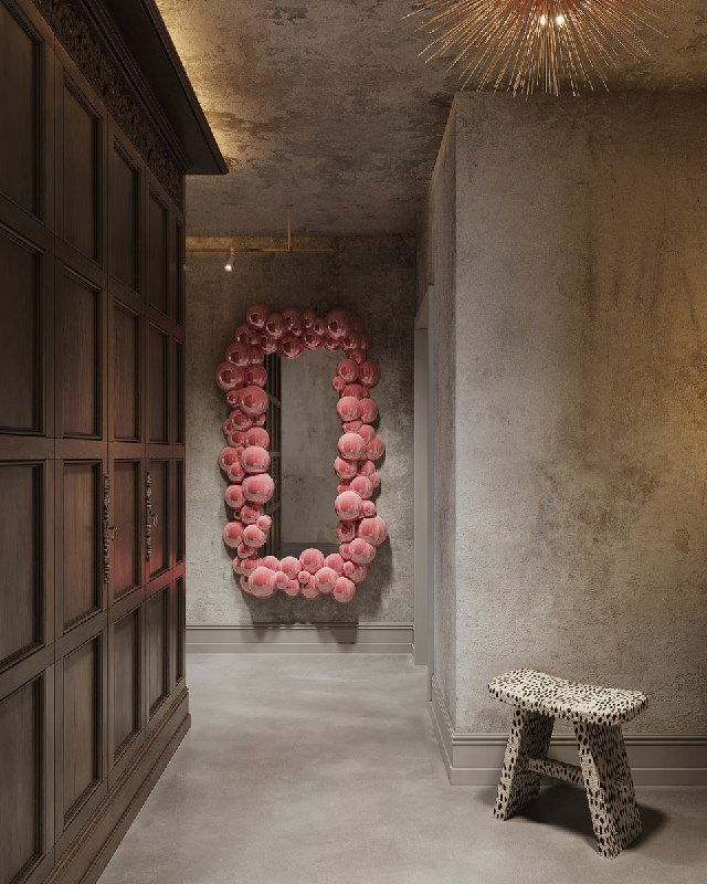 Вид вдоль прихожей на большое овальное зеркало в раме из розовых декоративных элементов, наливной бетонный пол и текстура состаренной штукатурки на стенах