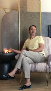 Мужчина в светлой футболке сидит в кресле в современной гостиной у декоративного очага и стеновой панели, виден интерьер зоны отдыха