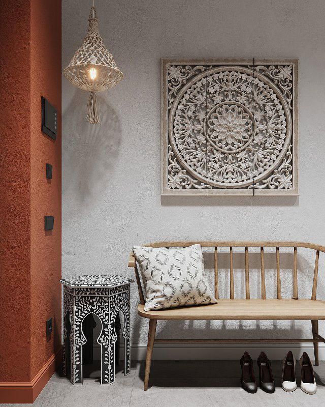 Крупный план уголка прихожей: этническая резная панель на светлой стене, деревянная скамейка с подушкой и декоративная лампа над ней.