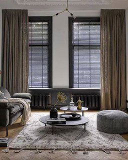 Комбинация штор и чёрных жалюзи в уютной гостиной с ковром и низким столом, мягкое рассеянное освещение создаёт атмосферу.