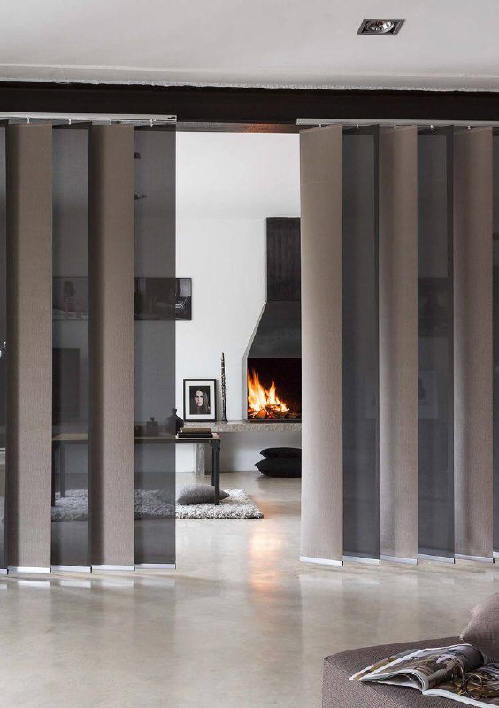 Современная гостиная с вертикальными японскими панелями между зонами, виден камин; серо-коричневая палитра и минимализм в планировке.