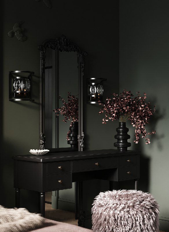 Буарный столик в тёмно‑зелёной комнате: чёрный комод с ящиками, большое резное зеркало, декоративные ветки в вазе и рядом меховой пуф.