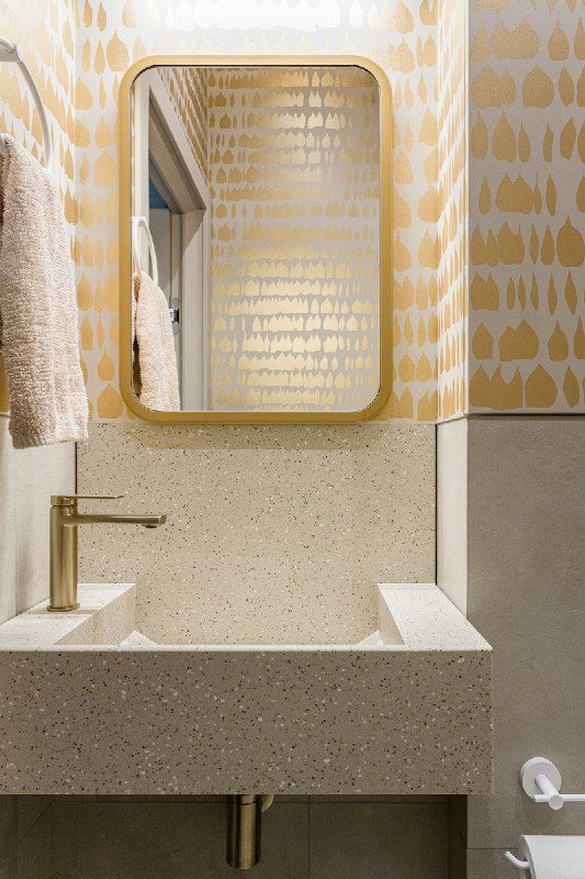 Миниатюрная раковина из искусственного камня по заказу, золотая смесительная арматура и зеркало в золотой раме на фоне художественного узора стен.