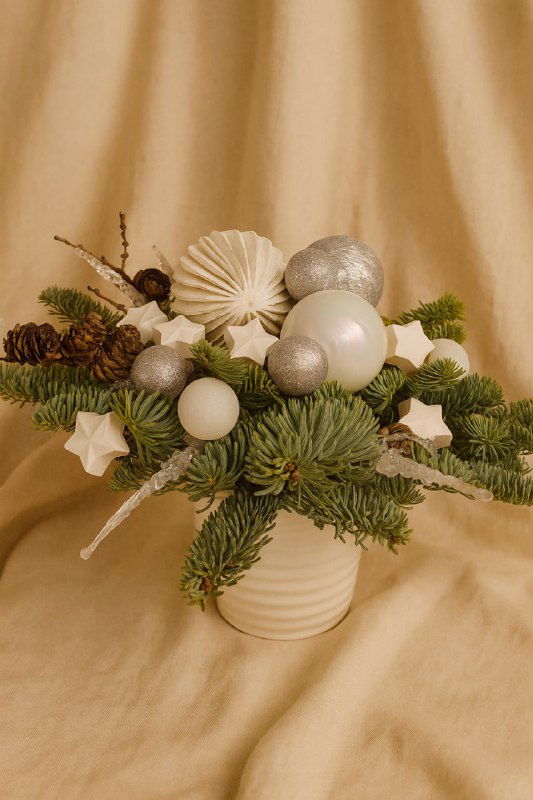 Низкая ваза с новогодней композицией из еловых веток, шишек и белых шаров на мягком бежевом фоне