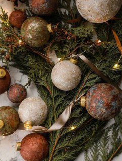 Фактурные шаровые ёлочные игрушки в тёплых коричневых и золотых тонах на хвое с гирляндой — идея сезонного декора и текстурных покрытий.