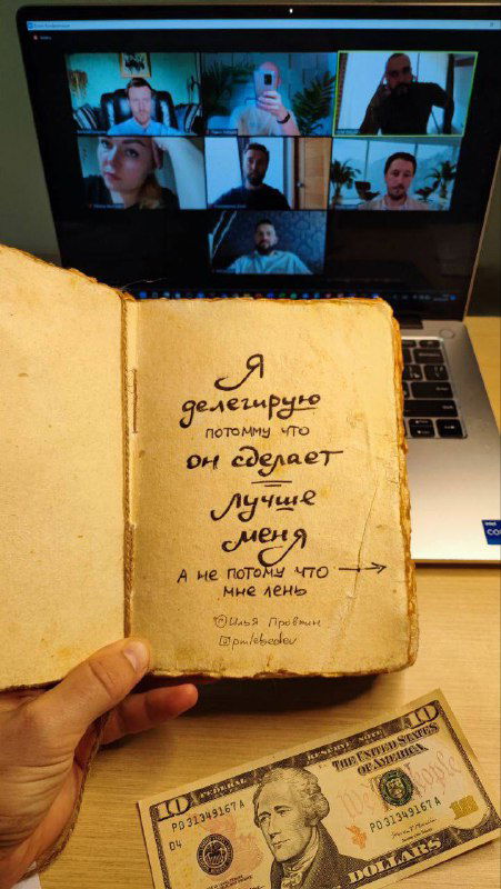 Тетрадь с мыслью о делегировании и купюрой на рабочем столе на фоне ноутбука с видеоконференцией — иллюстрация обсуждения найма.