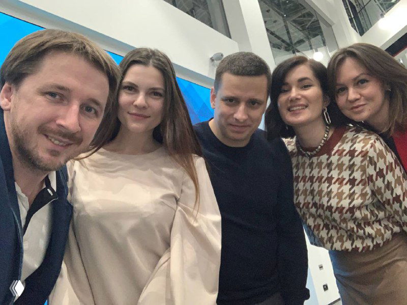 Групповое селфи команды и участников мероприятия в фойе: несколько улыбающихся людей в неформальной обстановке, атмосфера общения и нетворкинга.