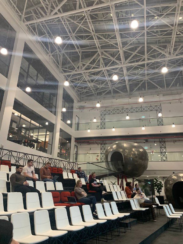 Зал с трибунами и высоким сводчатым потолком: пустые сиденья и архитектурное пространство места проведения демо‑дня в современном бизнес‑центре.