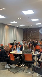 Группа участников сидит за столами в конференц-зале во время стратегической сессии; обсуждения и работа в командах видны на кадре.