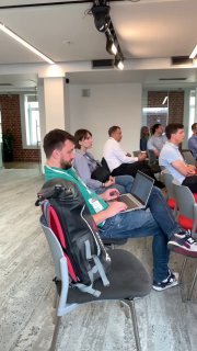 Слушатели на мероприятии: участники с ноутбуками и записными материалами, собрание в рабочем помещении с фокусом на обсуждение процессов и трекинга.