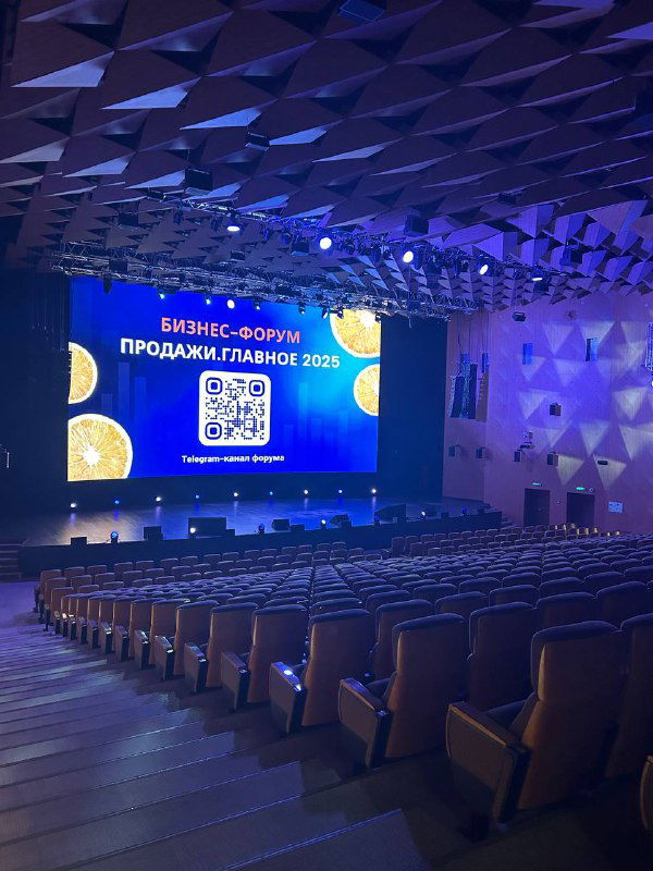 Внутренний вид конференц-зала с пустыми рядами кресел и большим экраном, оформленным в стиле делового форума «Продажи. Главное».