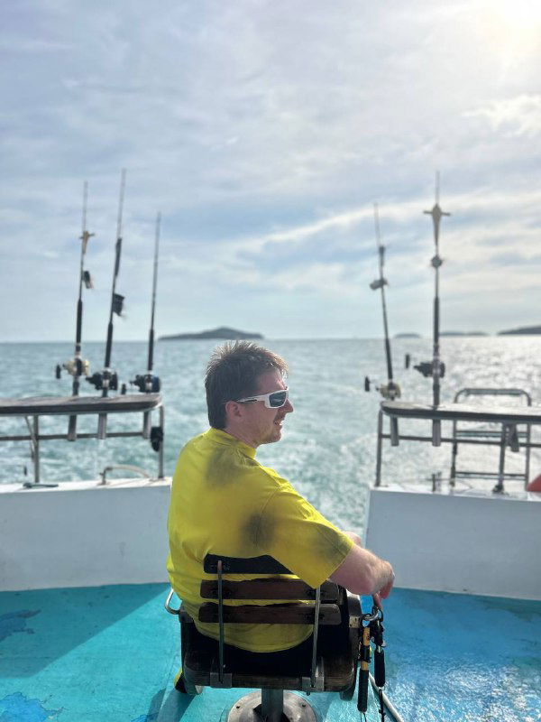 Человек в яркой футболке на палубе катера с видом на море и причалы на фоне — сцена спокойного путешествия и перезагрузки.