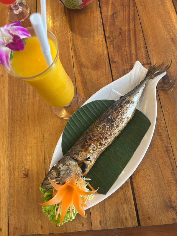 Тарелка с жареной рыбой и тропическим соком на деревянном столе — еда и окружение как часть восстановления во время поездки.
