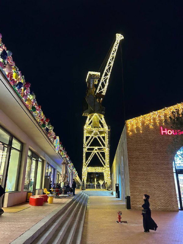 Ночная набережная или променада в Стамбуле с яркой иллюминацией, торговыми витринами и высоким краном на фоне — вечерний городской кадр.