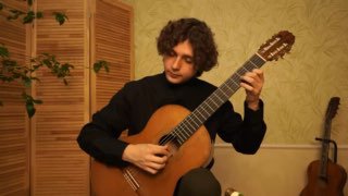 Сергей Гуделев играет на классической гитаре в комнате: видна посадка, положение рук и инструмент, демонстрирующие технику исполнения.