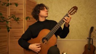 Классический гитарист в комнате исполняет пьесу — кадр из видео с демонстрацией позиции и техники для исполнения «Белый парус».