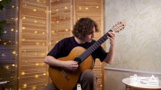 Гитарист сидит в домашней обстановке и играет на классической гитаре под мягкой подсветкой гирлянд — иллюстрация к пьесе и нотам.