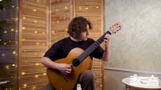 Музыкант играет на классической гитаре в уютной комнате с гирляндами на фоне; кадр иллюстрирует исполнение фольклорной пьесы и акцент на технике правой руки.