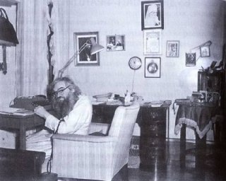 Черно‑белая фотография: святитель Иоанн Шанхайский дремлет в кресле за рабочим столом, вокруг иконы и церковные предметы, атмосферный кадр из кельи.