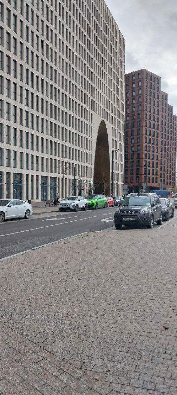 Современные фасады жилых кварталов ЗИЛАРТ с арочным проходом, улица и припаркованные машины на фоне урбанистического пространства.