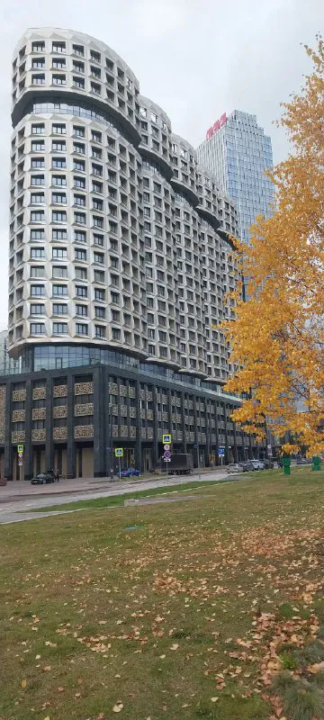 Округлые фасады и высокие дома в составе ЗИЛАРТ, осенние деревья и зелёная зона рядом с жилым комплексом.