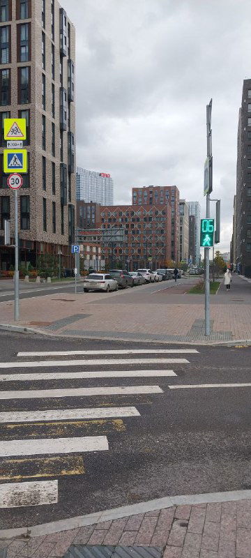 Перекрёсток и тротуар у жилого комплекса ЗИЛАРТ, дорожные знаки, пешеходный переход и городской пейзаж в пасмурный день.