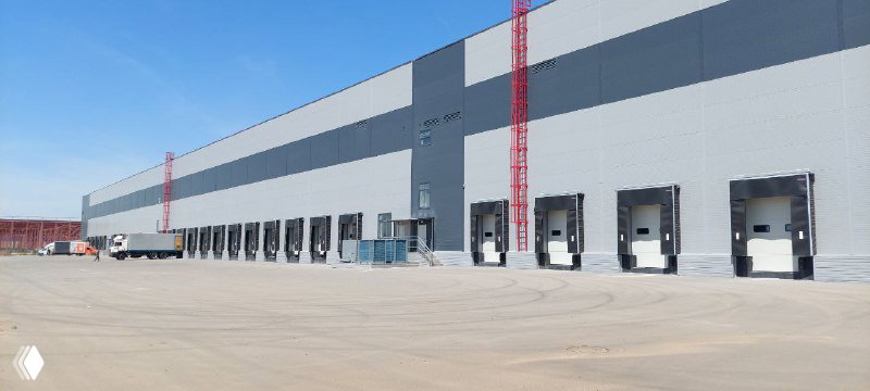 Фасад современного складского комплекса класса А в Астане с рядом доковых ворот, широкой въездной площадкой и пустой территорией для разгрузки
