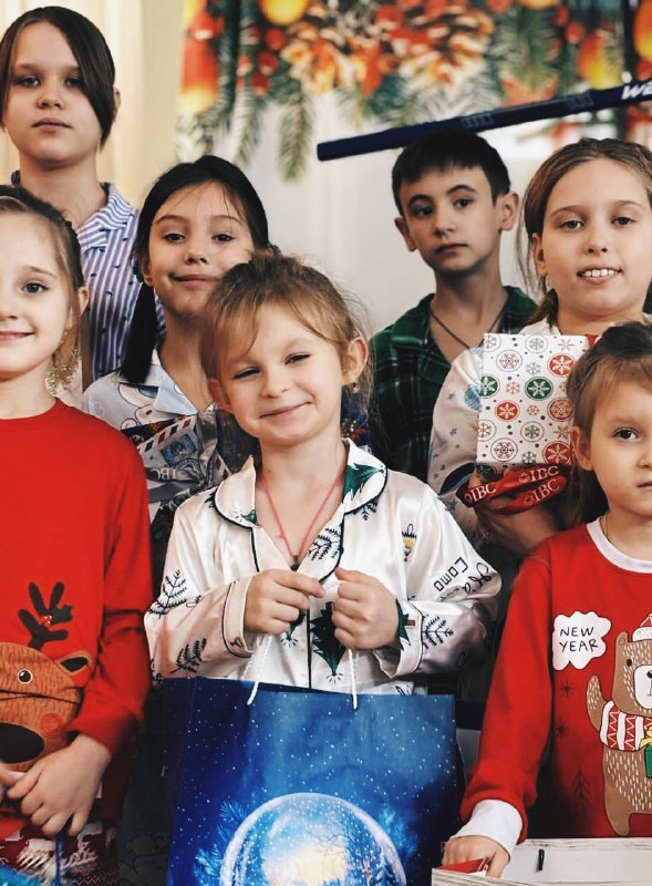 Крупный план улыбающихся детей из приюта при Троицком храме в Коломне с подарочными пакетами и коробками, вручёнными нашей командой.