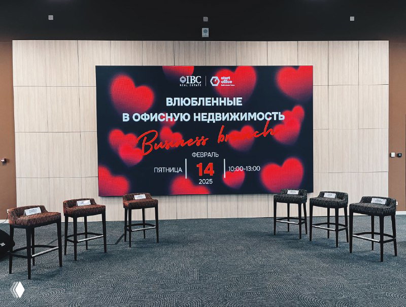 Зал с подготовленной сценой и большим экраном с анонсом «Влюбленные в офисную недвижимость» — место для бизнес‑бранча и прямых включений.