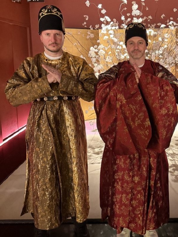Два мужчины в традиционных китайских костюмах позируют для фотографии в тематическом пространстве во время культурной программы.