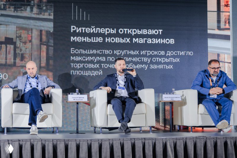 Трое спикеров на сцене во время сессии: каждый сидит в кресле, на экране за ними показаны слайды с аналитикой по ритейлу и торговым площадям.