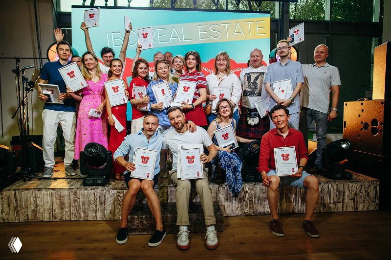 Групповое фото участников с призами и памятными сертификатами на сцене: сотрудники держат трофеи и улыбаются после закрытия спартакиады.