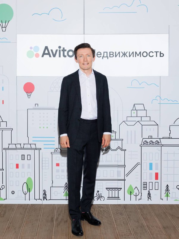 Артем Соломеннов позирует у брендволла Avito Недвижимость: официальная фотография спикера на фоне фирменной графики мероприятия.