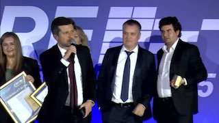 На сцене вручение награды: несколько человек в костюмах держат статуэтку и дипломы на фоне логотипа CRE Awards.