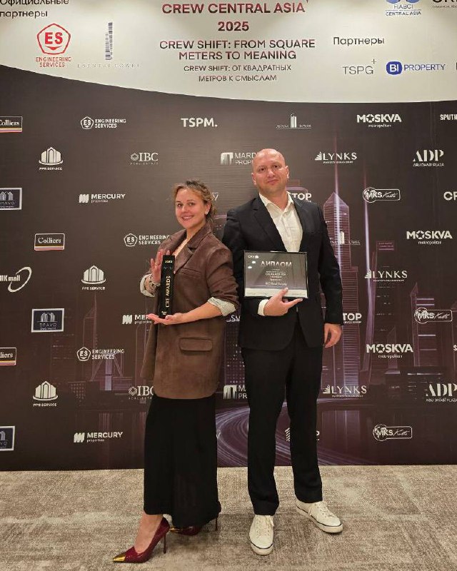 Двое сотрудников IBC Real Estate позируют с наградами на брендволле CREW Central Asia Awards 2025 в Алматы — момент церемонии.