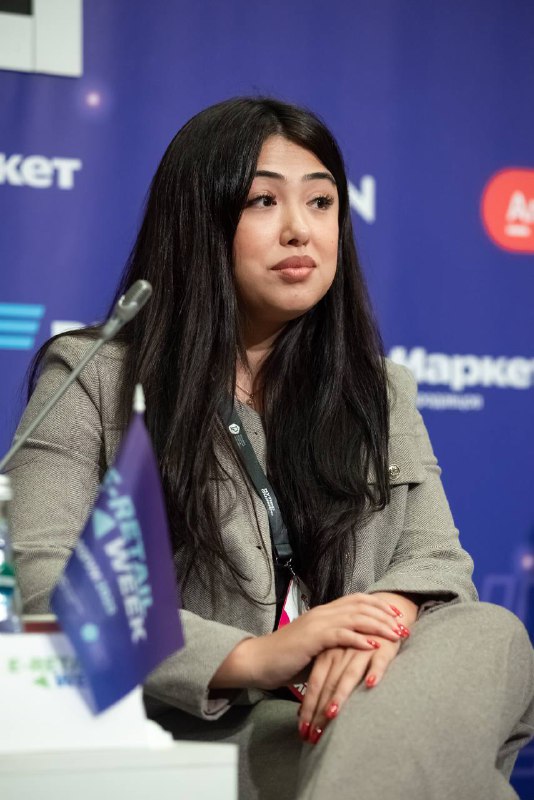 Портрет спикера в деловом костюме на сцене конференции E‑Retail Week; видна часть брендовой сцены и логотипы спонсоров.