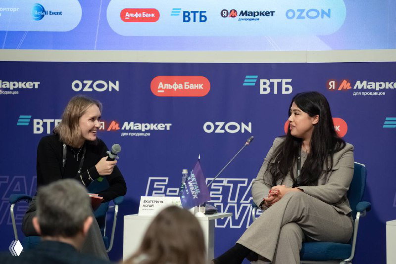 Два участника панельной дискуссии на сцене E‑Retail Week; спикеры ведут беседу на фоне брендированного баннера и логотипов.