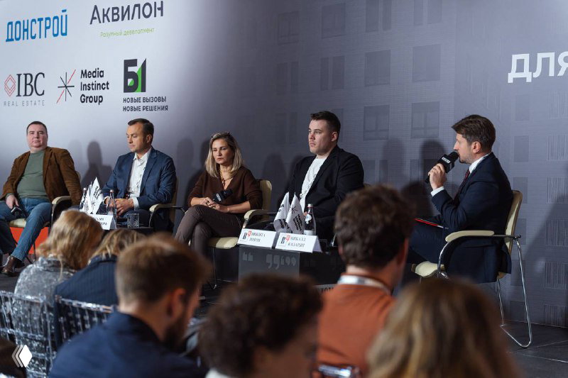 Широкий план панели и аудитории на XIX Московском форуме лидеров рынка недвижимости: гости в зале, спикеры на сцене и видимое брендирование организаторов и партнёров.