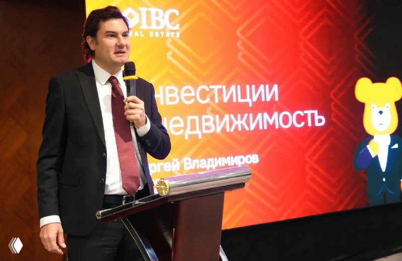 Сергей Владимиров на фоне большого экрана с презентацией «Инвестиции в недвижимость», кадр показывает логотип IBC и название доклада.